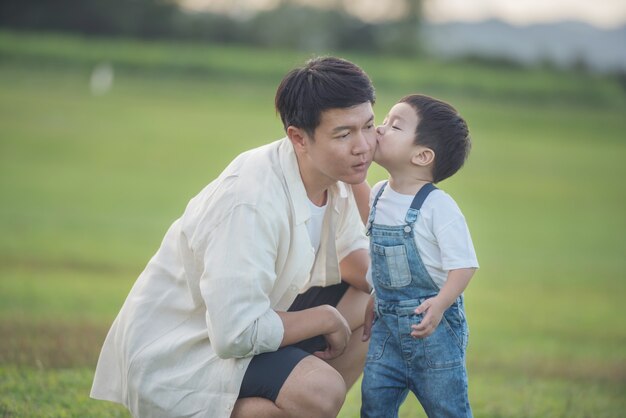 아버지와 아들이 일몰 시간에 공원에서 연주. 사람들은 현장에서 재미. 친절한 가족과 여름 휴가의 개념. 아버지와 아들 다리 공원에서 잔디밭을 가로 질러 걸어