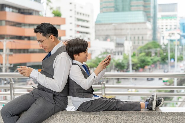 都市のビジネス地区で一緒にスマートフォンをプレイする父と息子