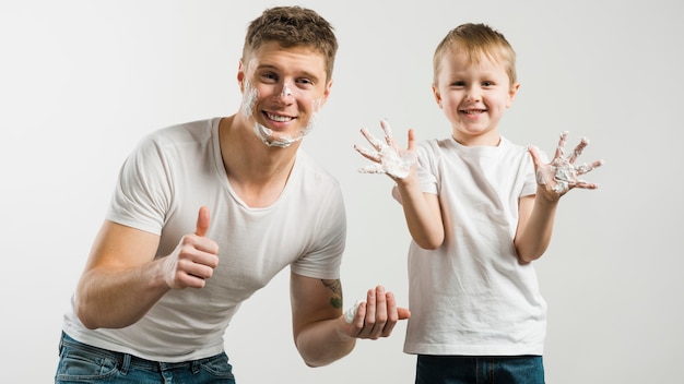 Father and son playing with shaving foam showing thumb up sign against white backdrop
