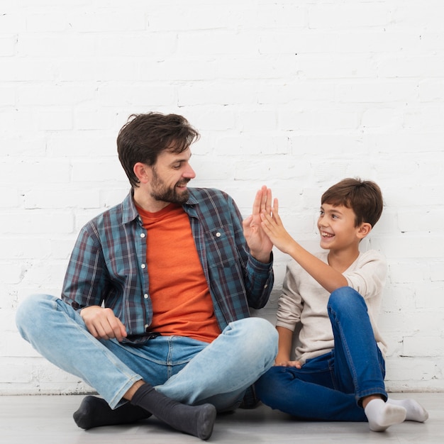 Father and son sitting on floor and high five