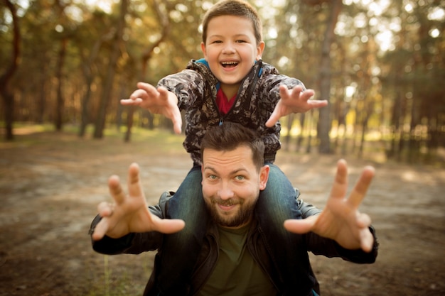 Father and son walking and having fun in autumn forest, look happy and sincere