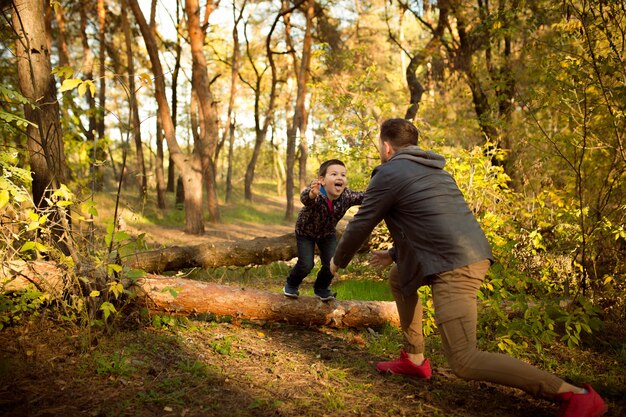 Отец и сын гуляют и веселятся в осеннем лесу, выглядят счастливыми и искренними