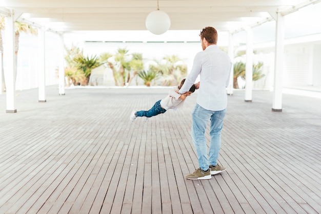 Free photo father swinging child by arms on beachfront