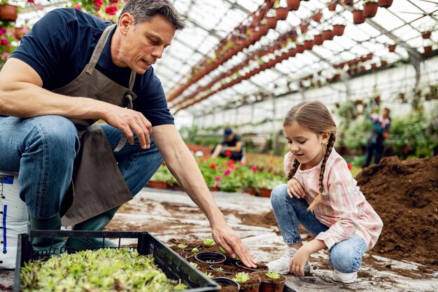 Отец учит свою маленькую дочь сажать цветы в питомнике растений