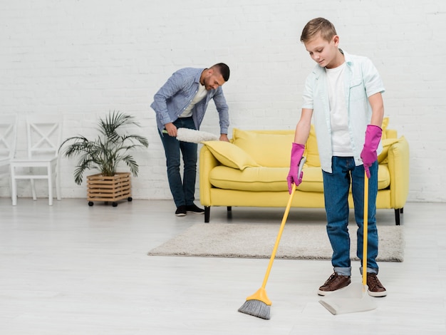 Father using duster while son uses broom