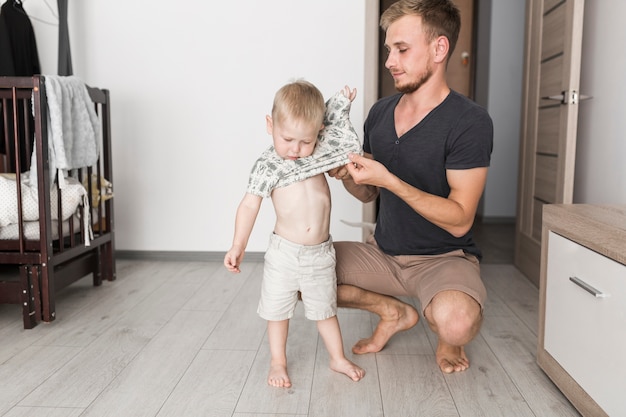 Foto gratuita padre che indossa la maglietta per il suo piccolo figlio a casa