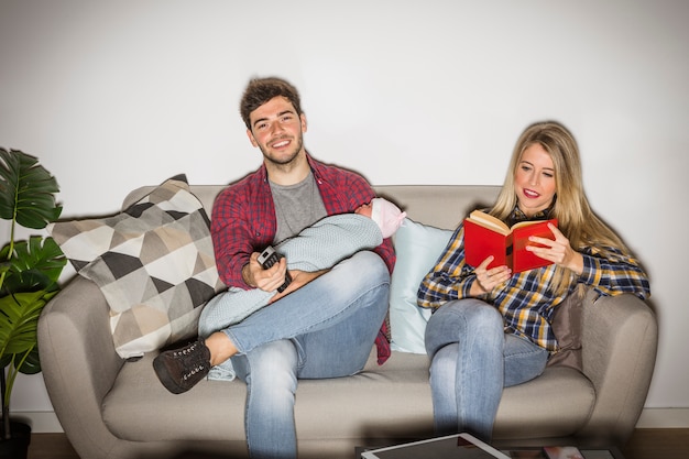 Father with baby watching TV while mother reading book