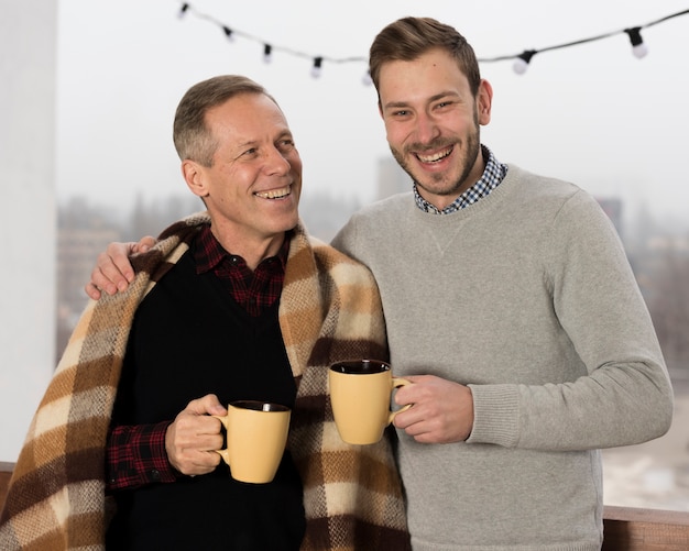 Father with blanket posing with son while holding cups in hands