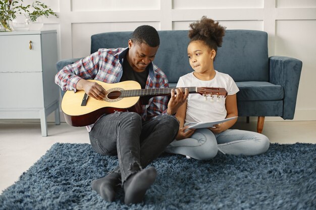ソファの上に娘を持つ父。ギターを持っている女の子。ギターを学ぶ。