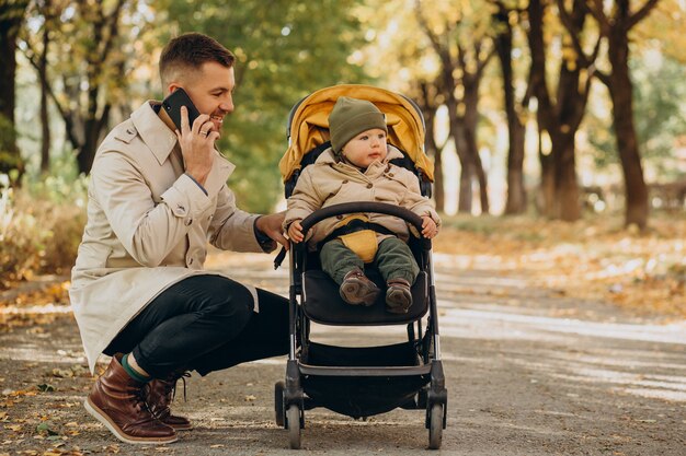 Father with little son walking in baby stroller in autumnal park