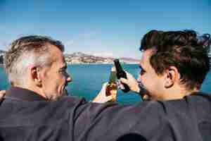 Foto gratuita concetto di giorno di padri con padre e figlio brindando con la birra di fronte acqua