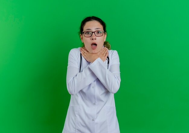 Fed up young female doctor wearing medical robe and stethoscope and glasses  choking herself isolated on green wall with copy space