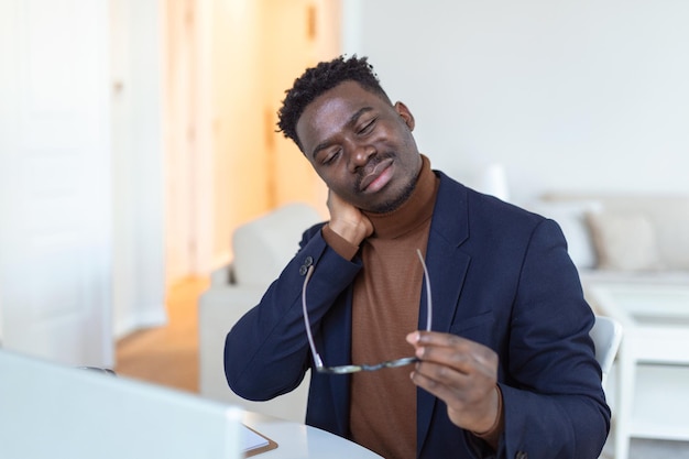 Feeling exhausted Frustrated young handsome man looking exhausted while sitting at his home and working on his laptop while massaging his neck Neck pain