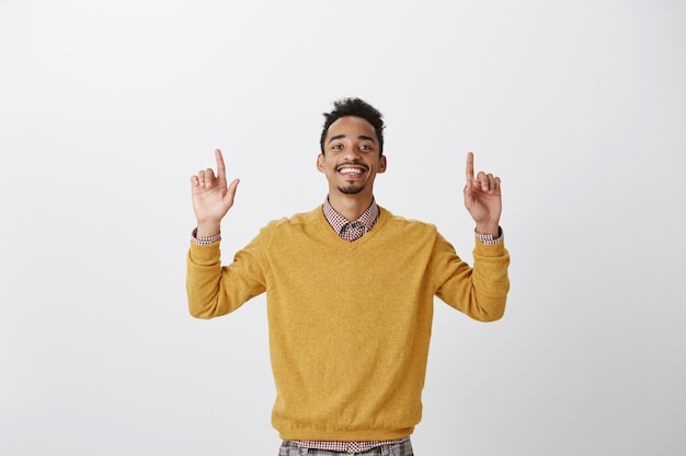 승자 같은 느낌. 노란색 풀오버에 만족 한 행복한 아프리카 계 미국인 남자의 초상화, 검지 손가락을 들고 위쪽을 가리키고, 긍정적 인 결과에 만족하고, 좋은 소식에서 승리