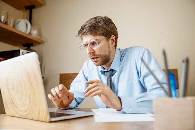 Feeling sick and tired. Frustrated sad unhappy sick young man massaging his head while sitting at his working place in office. The seasonal flu, pandemic influenza, disease prevention concept