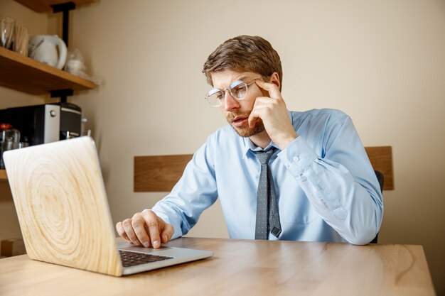 Feeling sick and tired. Frustrated sad unhappy sick young man massaging his head while sitting at his working place in office.