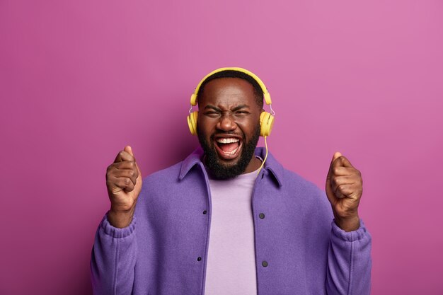 Sensazione di successo. l'uomo con la barba lunga positivo sta con i pugni alzati, ride felice, ascolta la canzone preferita in cuffia durante il tempo libero