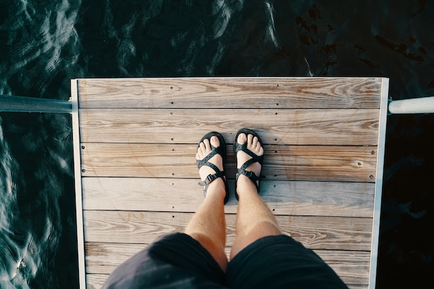 Free photo feet of a male standing on a wooden surface over the body of water