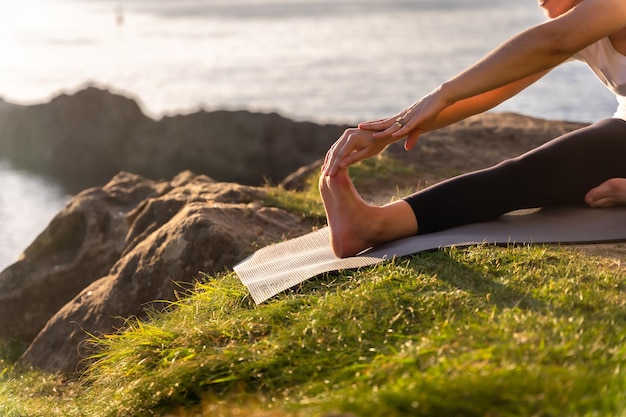 灯台の横に広がる海沿いの自然の中でヨガの練習をしている女性の足は、健康で裸体主義者の生活屋外ピラティス
