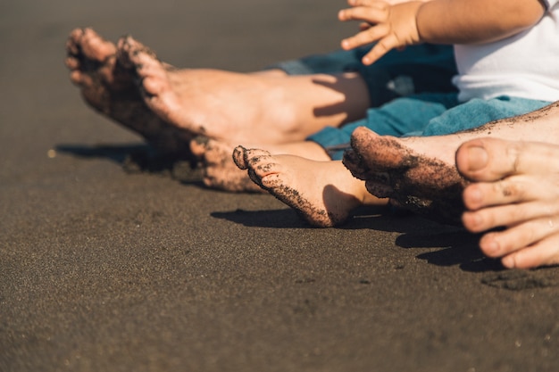 Feet of parents and baby sitting on sandy beach