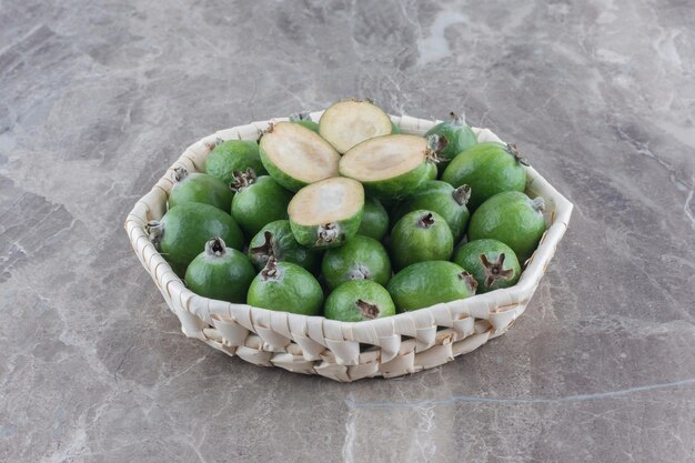 Feijoa piled in a white basket and adorned with feijoa slices on marble surface