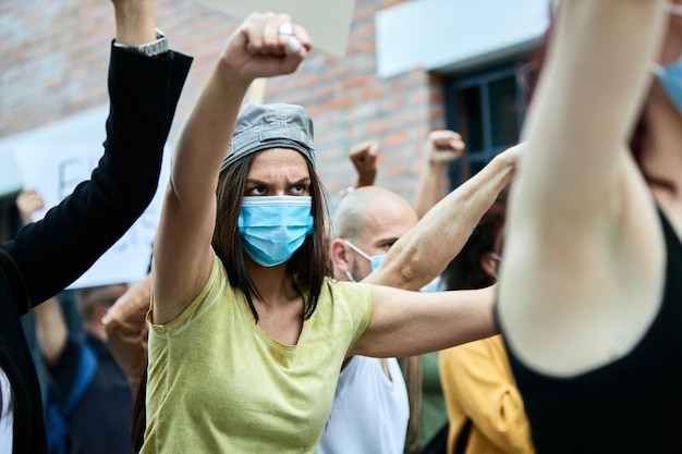 Female activist wearing protective face mask while protesting with crowd of people during COVID19 pandemic