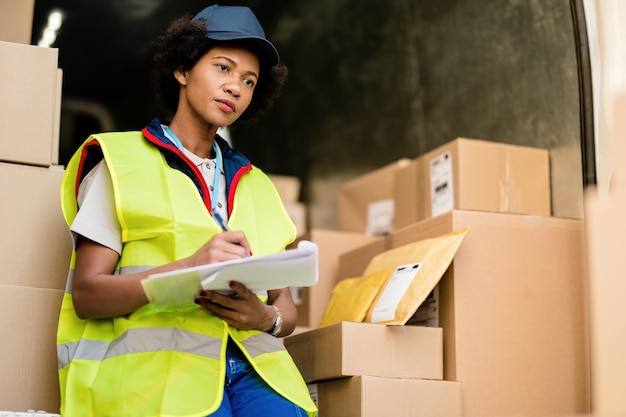 Female African American courier thinking while going through delivery schedule list in a delivery van