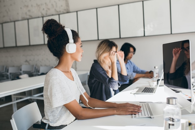 Female african call center employee using computer and talking with co-workers. Indoor portrait of managers of international company working in big office.