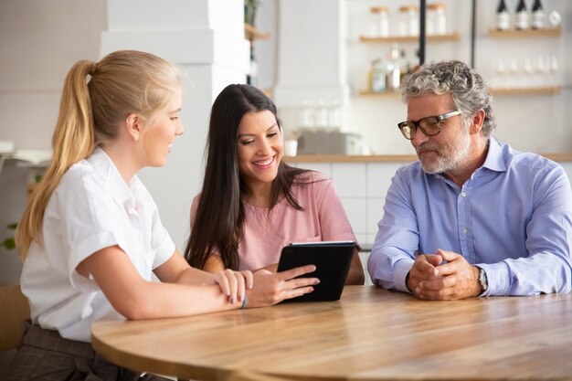 Female agent or manager meeting with couple of young and mature customers, presenting content on tablet