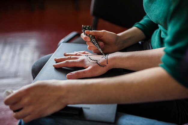 A female applying mehndi tattoo over the woman's hand