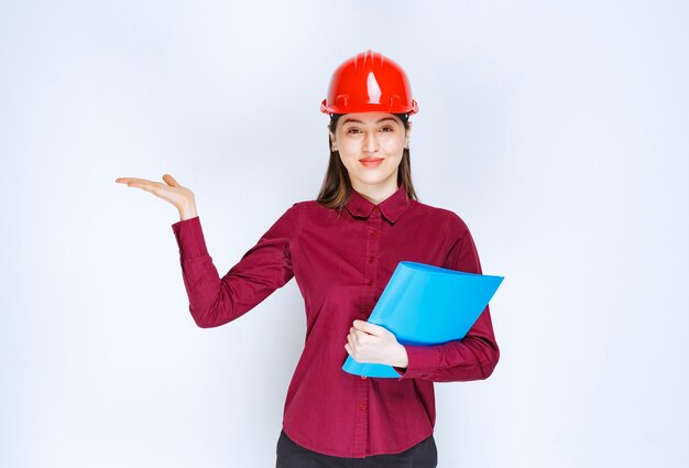 Female architect in red helmet with blue folder getting standing and posing. 