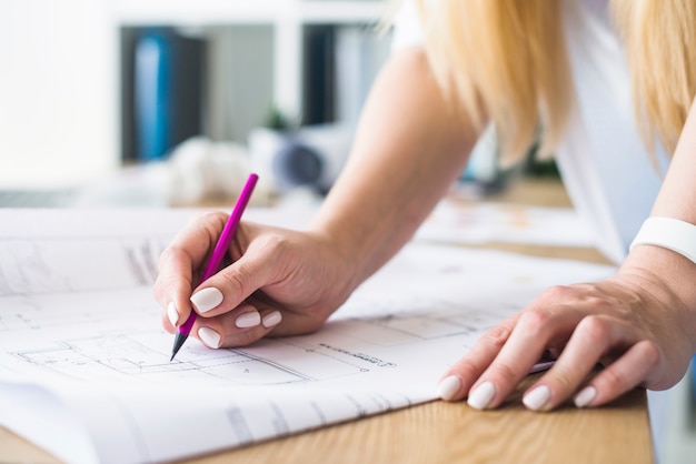 Female architect's hand drawing blueprint over wooden desk