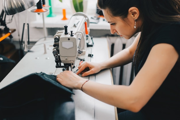 Female artisan threading black leather on sewing machine