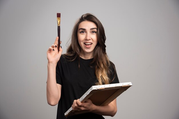 Female artist in black shirt holding artistic tools. 