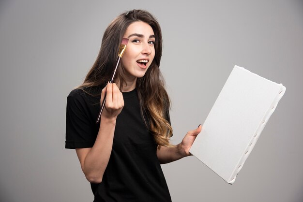 Female artist in black shirt using brush for her face. 