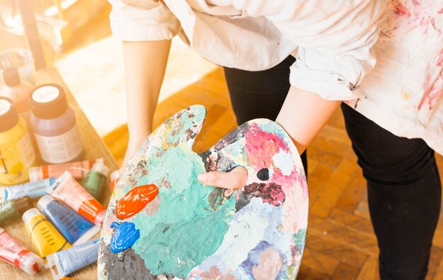 Female artist's hand holding messy paint palette at workshop