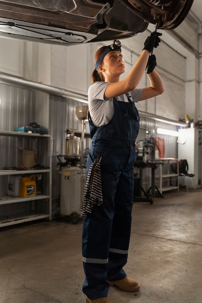 Free photo female auto repairer working in the shop on a car