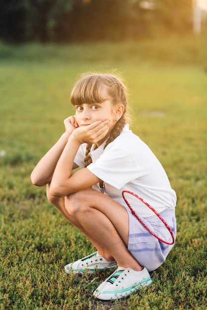 Female badminton player crouching on green grass