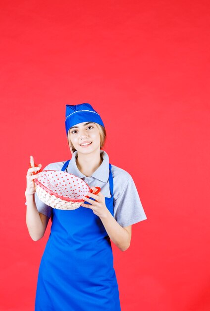 파란 앞치마를 입은 여성 제빵사, 안에 빨간 수건이 든 빵 바구니를 들고