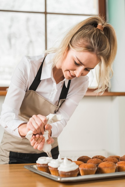 アイシングバッグを絞ることによって白いバタークリームとケーキを飾る女性のパン屋