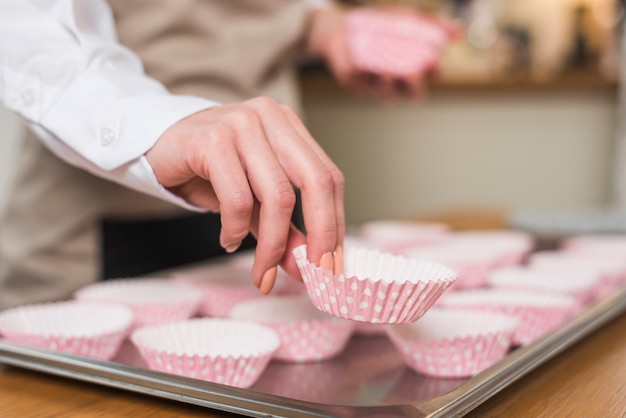 Female baker's hand placing the cupcake case on the tray