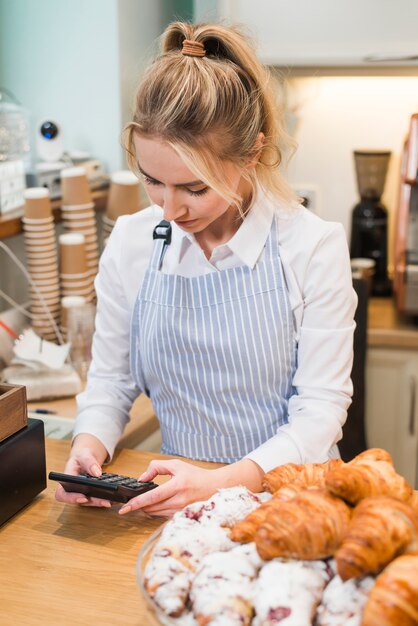Female baker standing in her coffee shop using the calculator