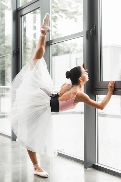 Female ballerina stretching her leg near the window