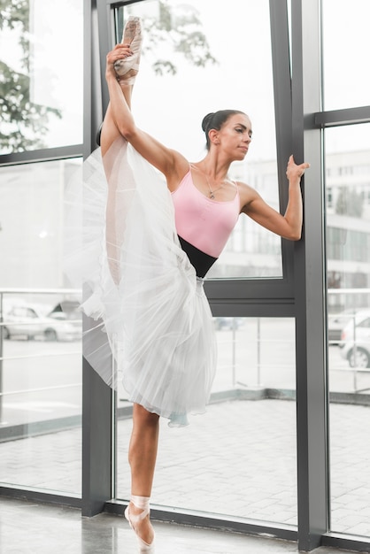 Female ballerina stretching her leg near the window