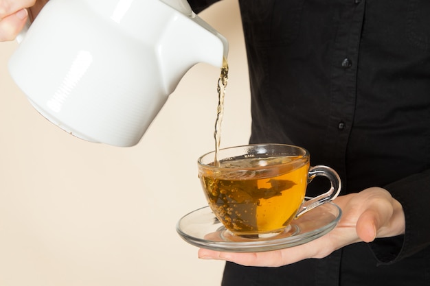 白い壁にお茶を作るコーヒーブラウン乾燥茶機器成分と黒いシャツズボンの女性バリスタ