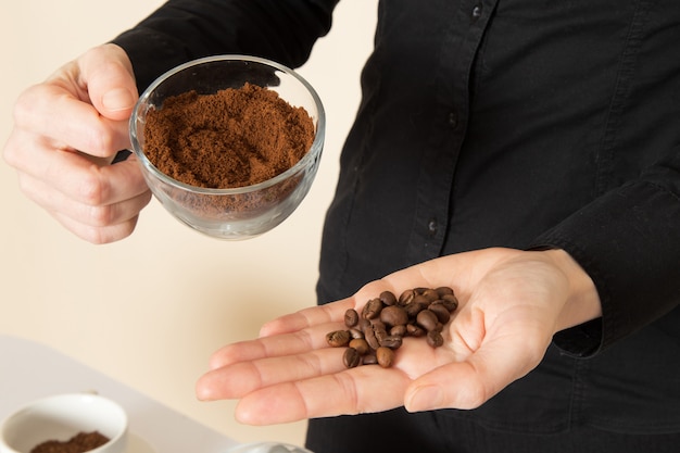 Foto gratuita barista femmina in pantaloni camicia nera con caffè marrone essiccato ingredienti attrezzature tè sul muro bianco