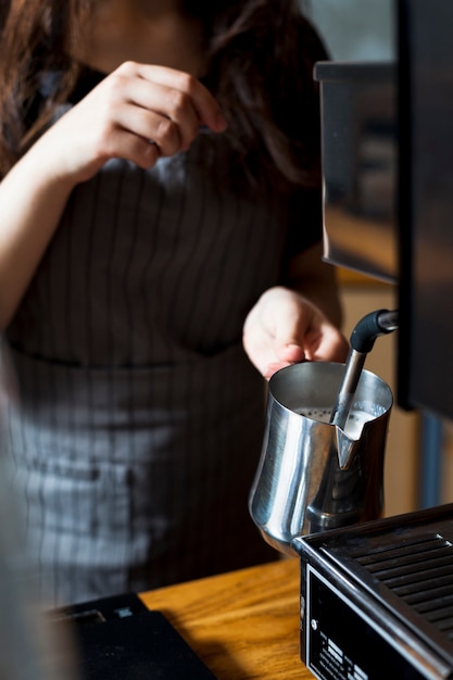 Female barista hand steaming milk for latte in stainless steel pitcher