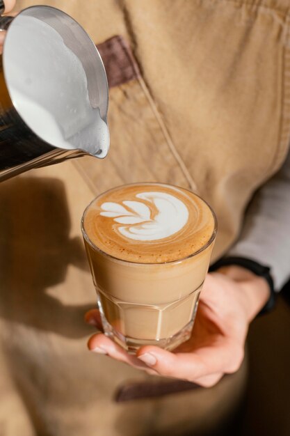 牛乳でコーヒーガラスを飾るエプロンと女性のバリスタ