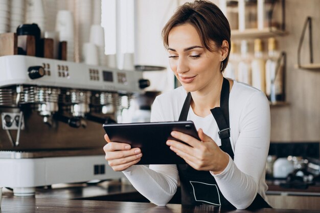 コーヒーショップで注文するタブレットを持つ女性のバリスタ