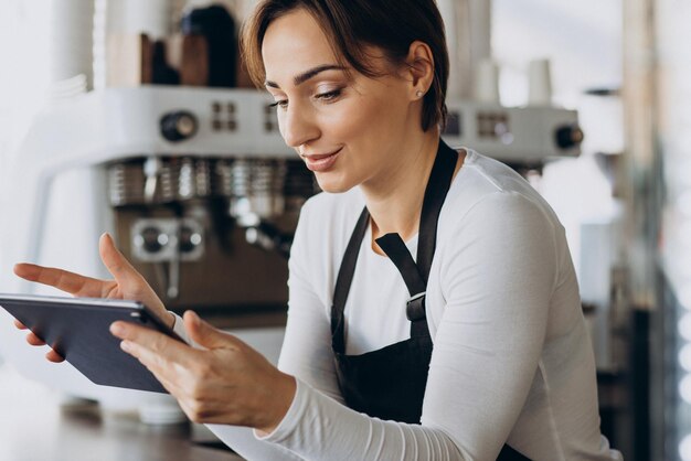 コーヒーショップで注文するタブレットを持つ女性のバリスタ